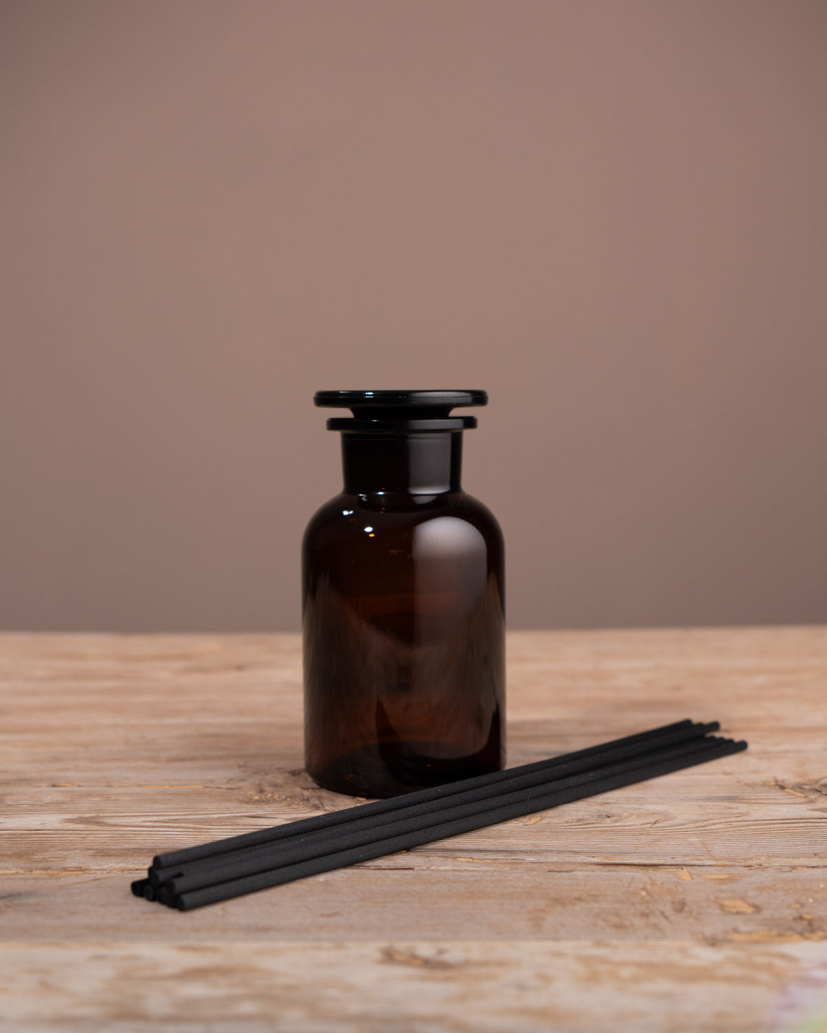Brown glass diffuser bottle with black reeds on a wooden surface against a brown background