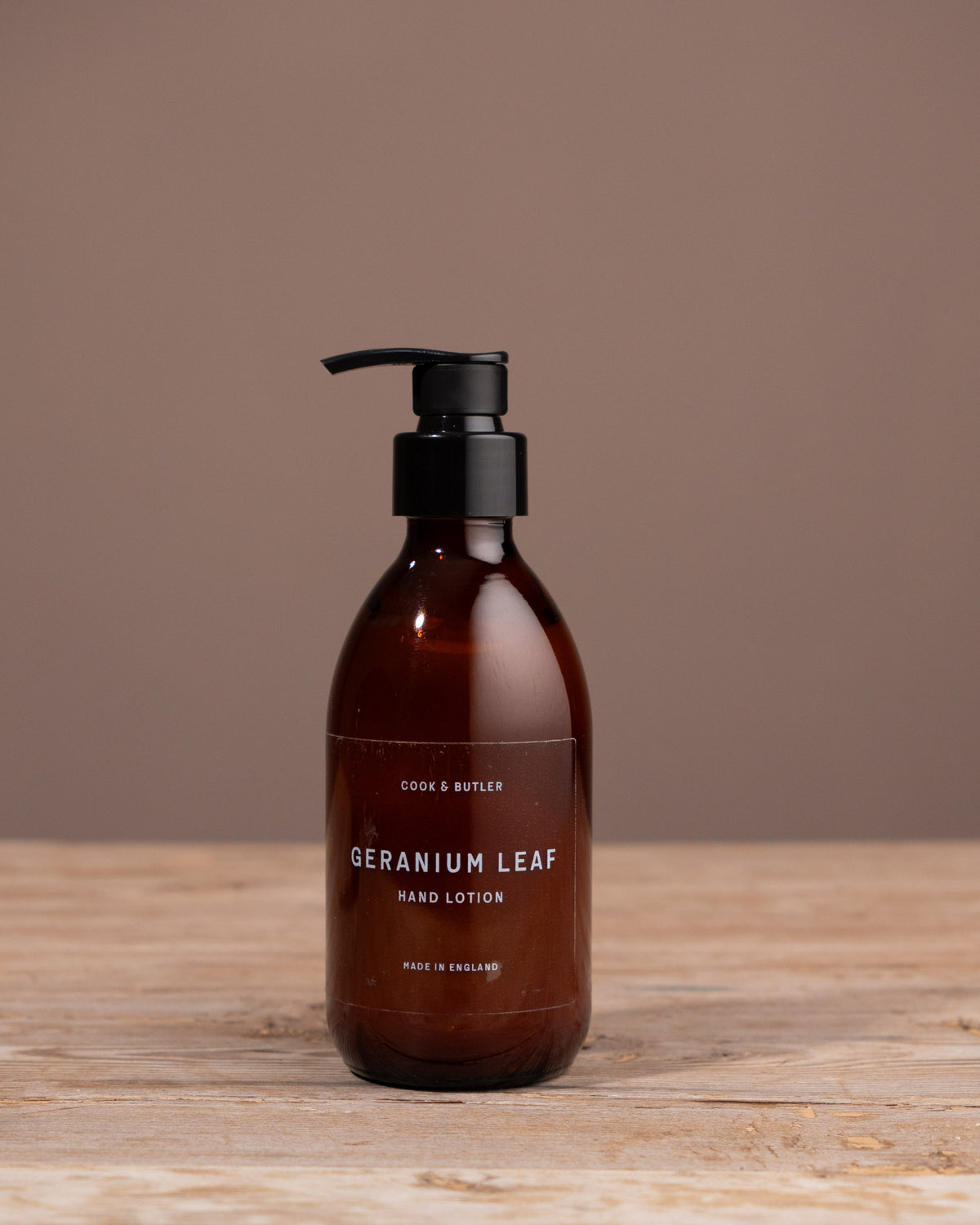 Cook & Butler hand lotion bottle with pump on a wooden surface and brown background