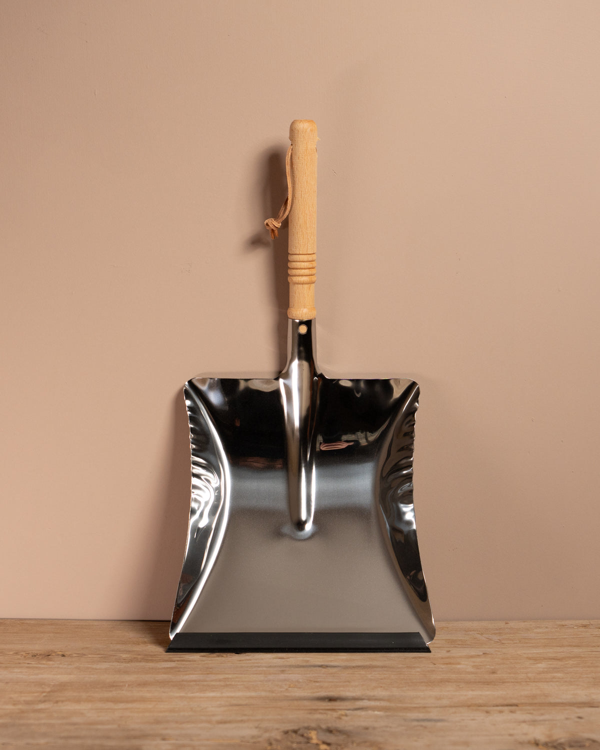 Metal dust shovel with wooden handle on a wooden surface and beige background