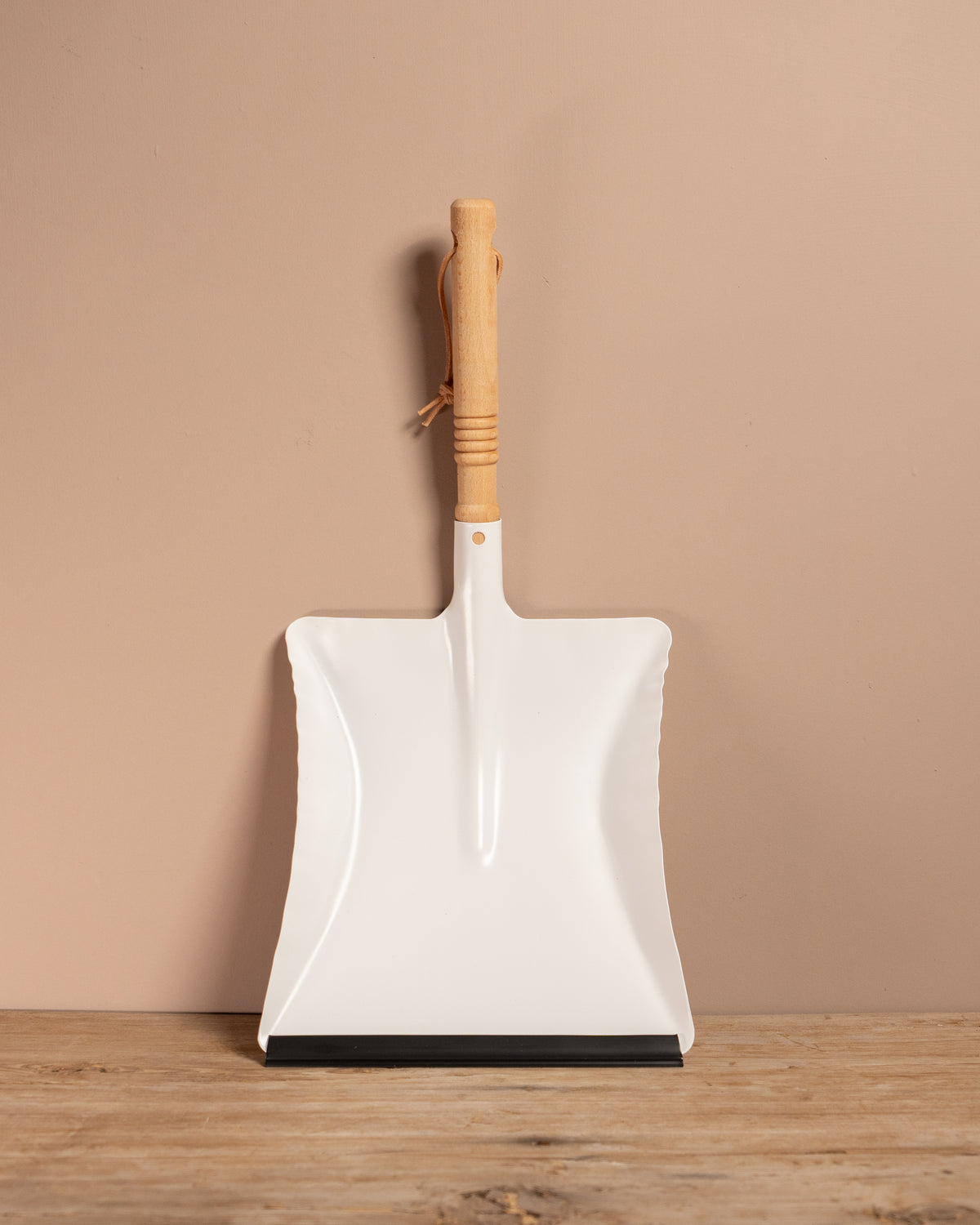 White dust shovel with wooden handle on a beige background