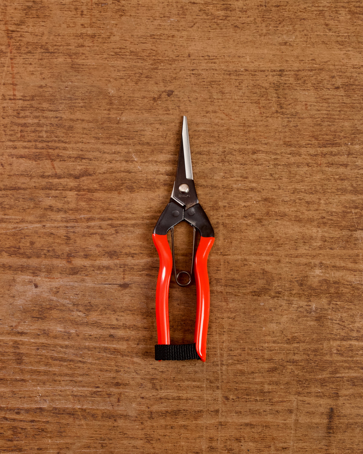 Pair of garden snips with red handles on a wooden surface