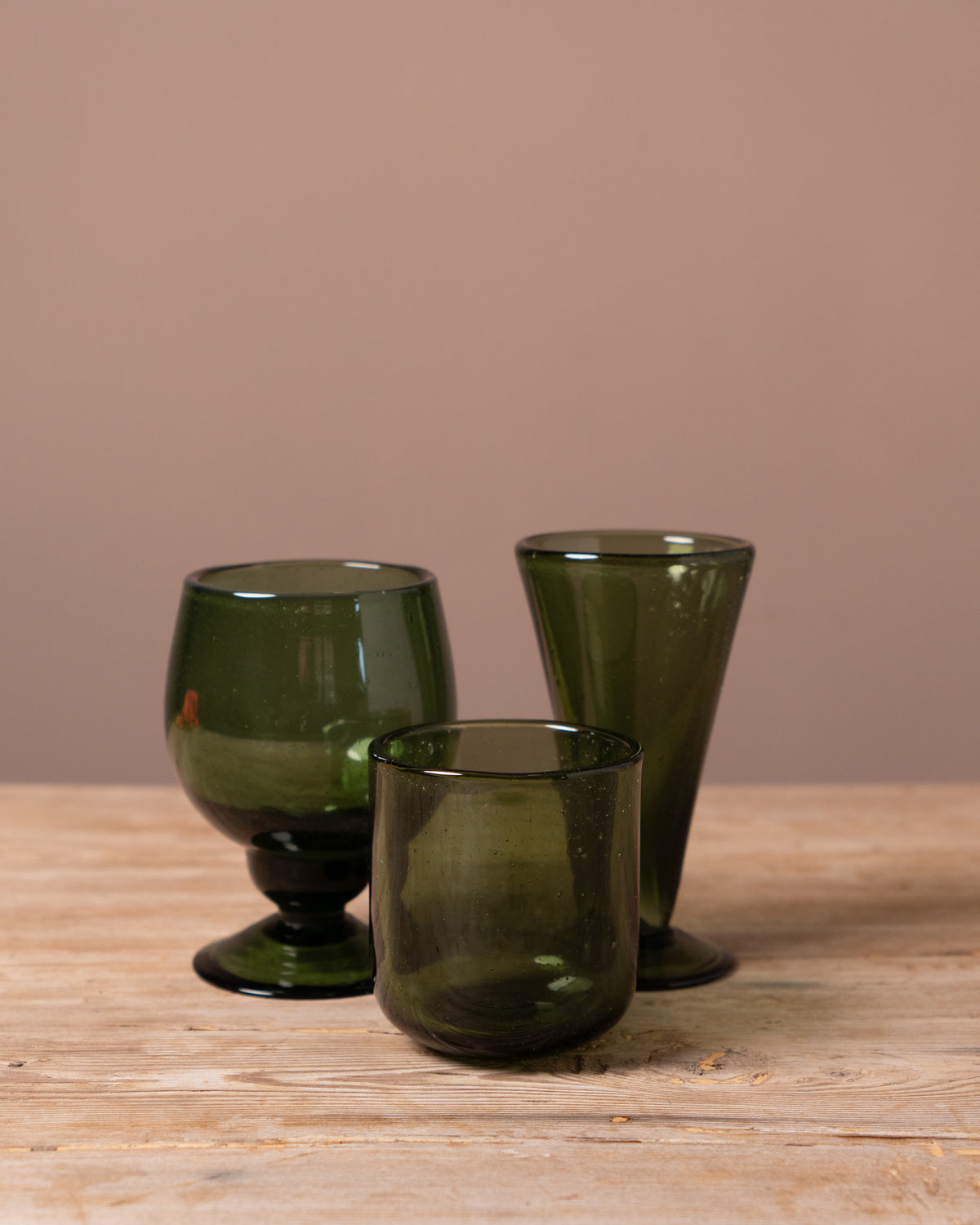 Three green glass tumblers on a wooden surface with a beige background