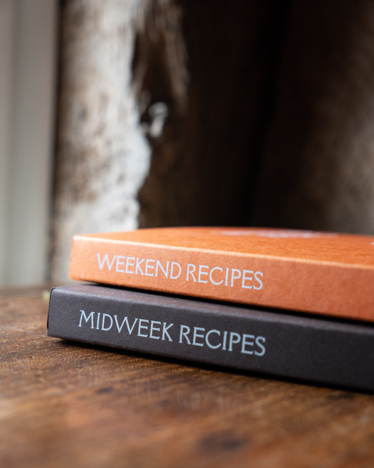 Two recipe books titled 'Midweek Recipes' and 'Weekend Recipes' on a wooden surface.