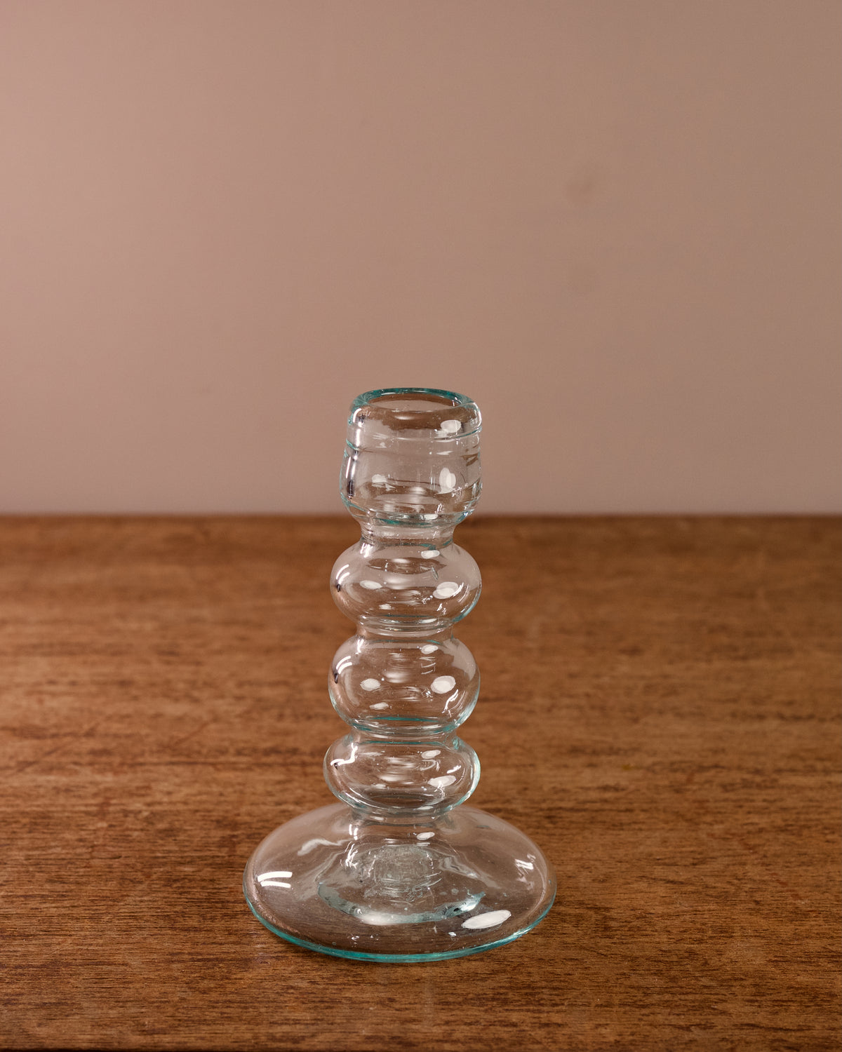 Clear glass candlestick on a wooden surface with a beige background