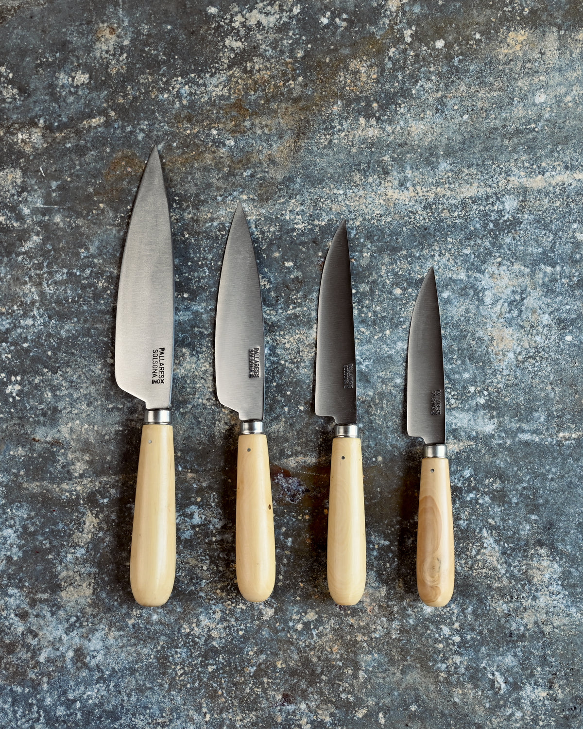 Set of four knives with wooden handles on a textured stone surface