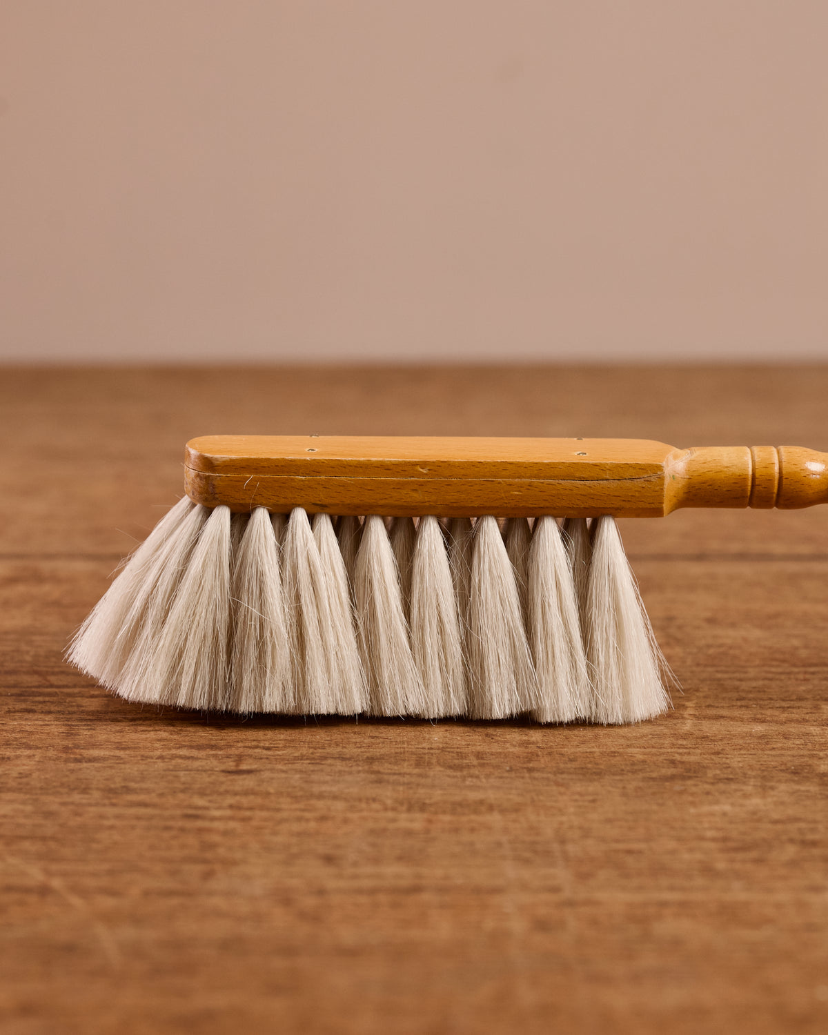 Wooden cleaning brush with white bristles on a wooden surface