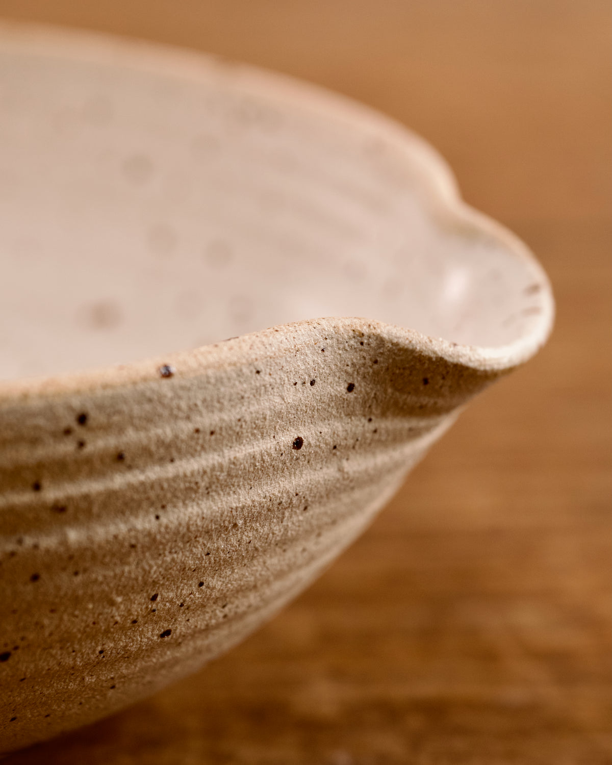 Speckled ceramic mixing bowl on a wooden surface with a beige background
