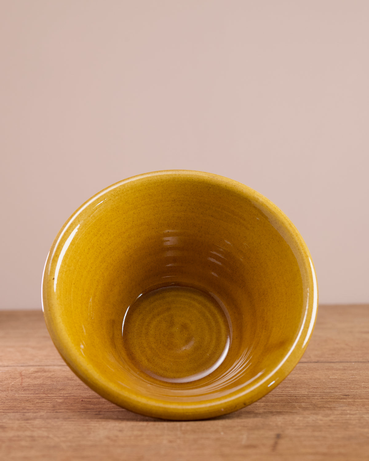 Terracotta bowl with yellow glazed interior on a wooden surface.