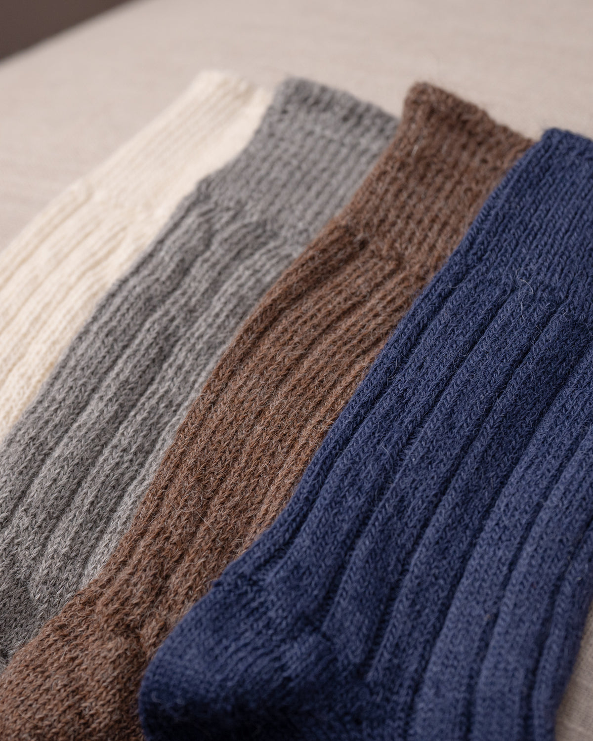 Four pairs of knitted socks in white, grey, brown, and blue on a light background.