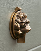 Brass keyhole cover shaped like a lion's head on a light grey door.