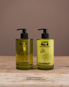 Two bottles of C.atherley Geranium No. 4 hand and body lotion on a wooden surface with a brown background.