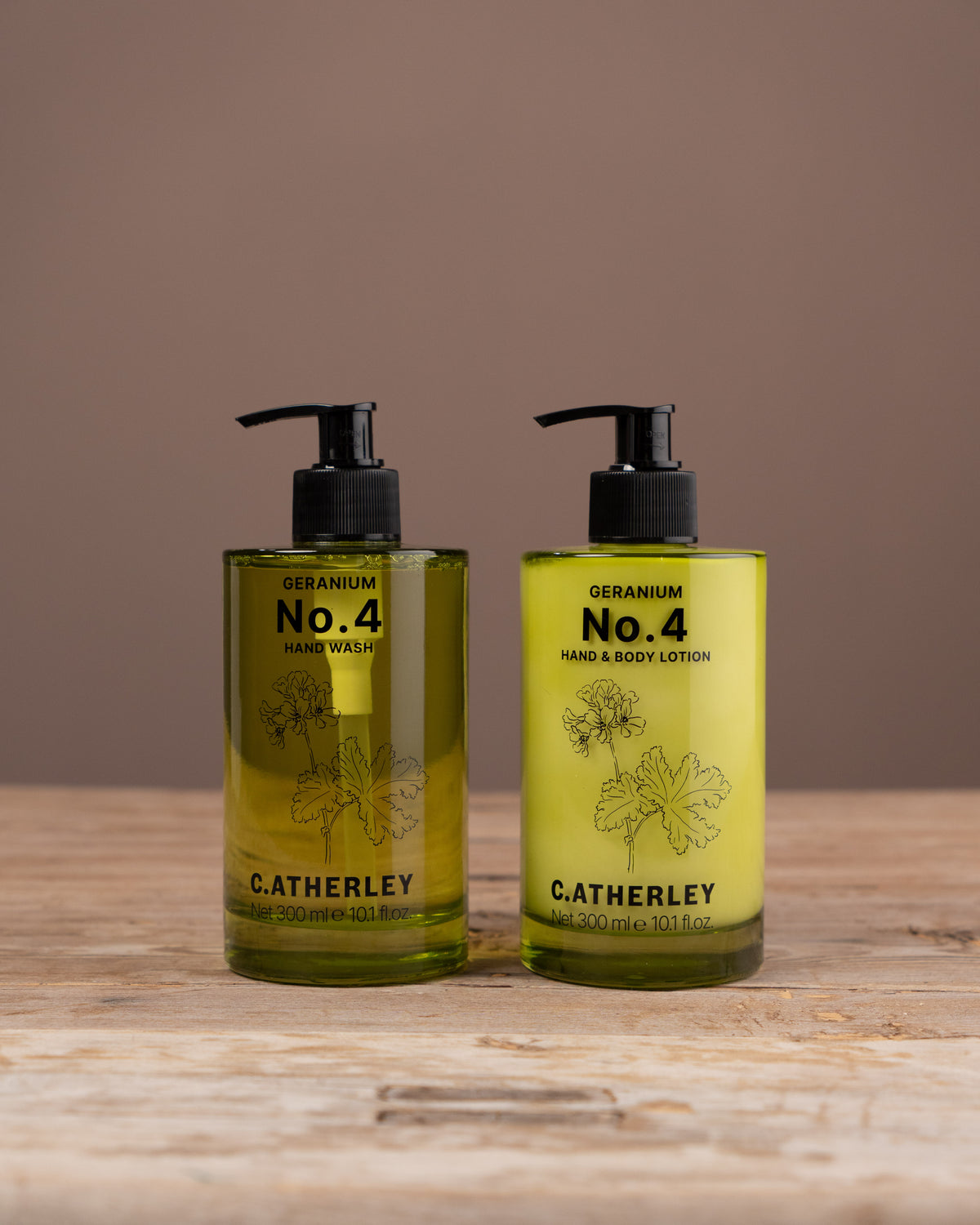 Two bottles of C.atherley Geranium No. 4 hand and body lotion on a wooden surface with a brown background.
