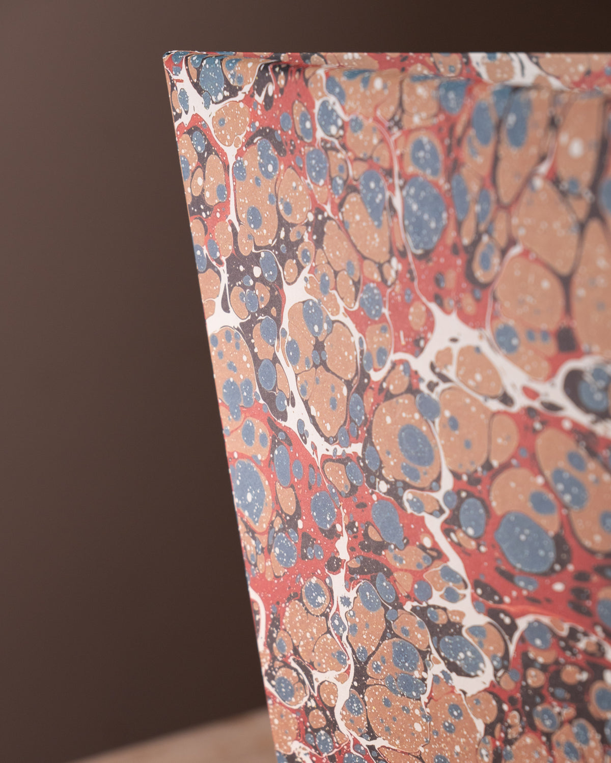 Marbled paper with red, blue, and beige pattern on a dark background