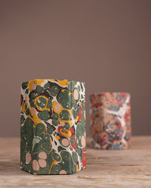 Two cylindrical containers with colorful marbled patterns on a wooden surface and brown background