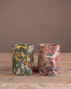 Two patterned pen pots on a wooden surface with a brown background