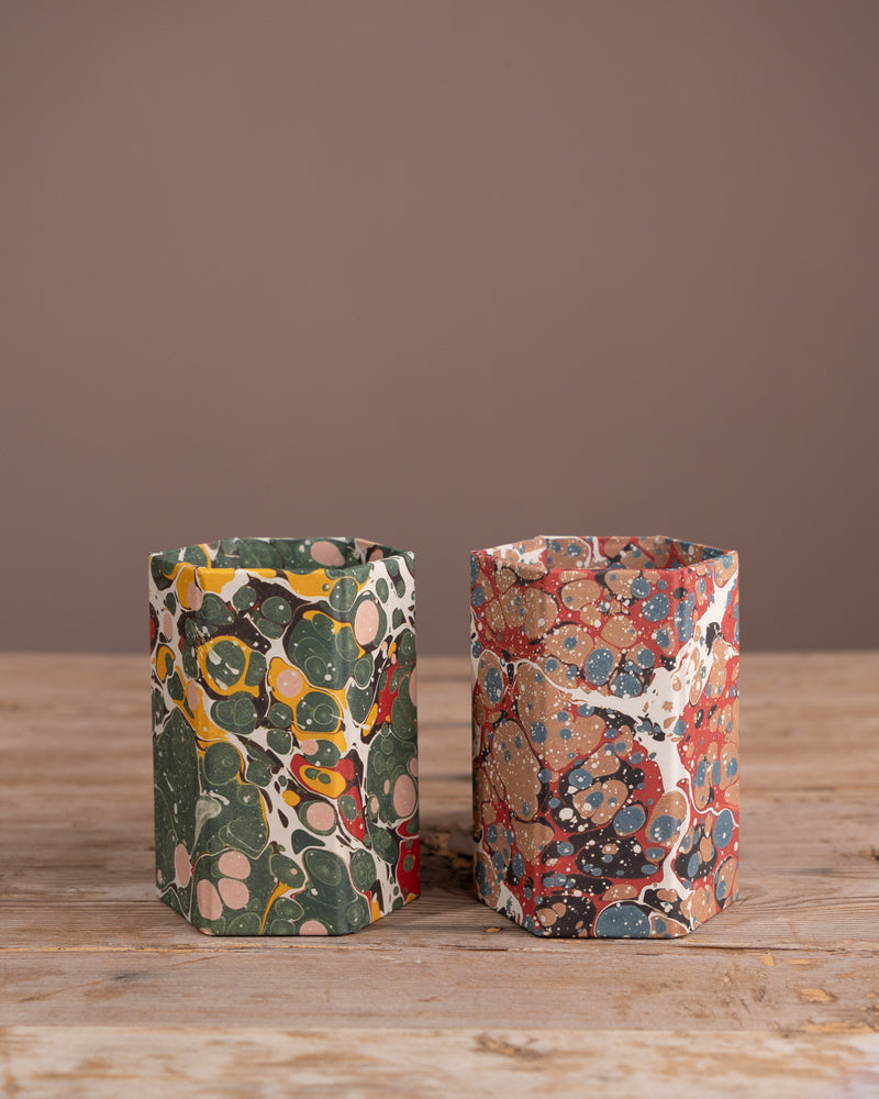 Two patterned pen pots on a wooden surface with a brown background