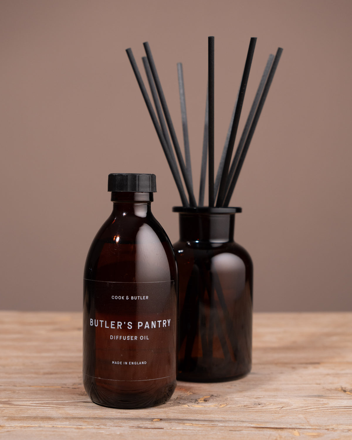 Brown diffuser oil bottle with black reeds on a wooden surface against a brown background