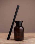 Brown diffuser bottle with black reeds on a wooden surface and brown background