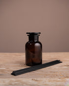 Brown glass diffuser bottle with black reeds on a wooden surface against a brown background