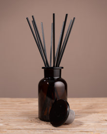 Brown diffuser bottle with black sticks on a wooden surface and brown background