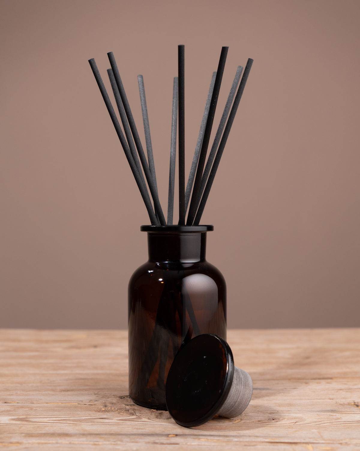Brown diffuser bottle with black sticks on a wooden surface and brown background