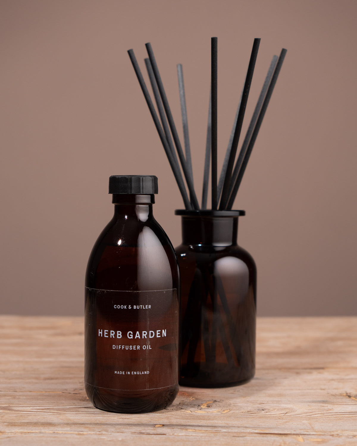 Brown diffuser bottle with black label and black reeds on a wooden surface against a brown background