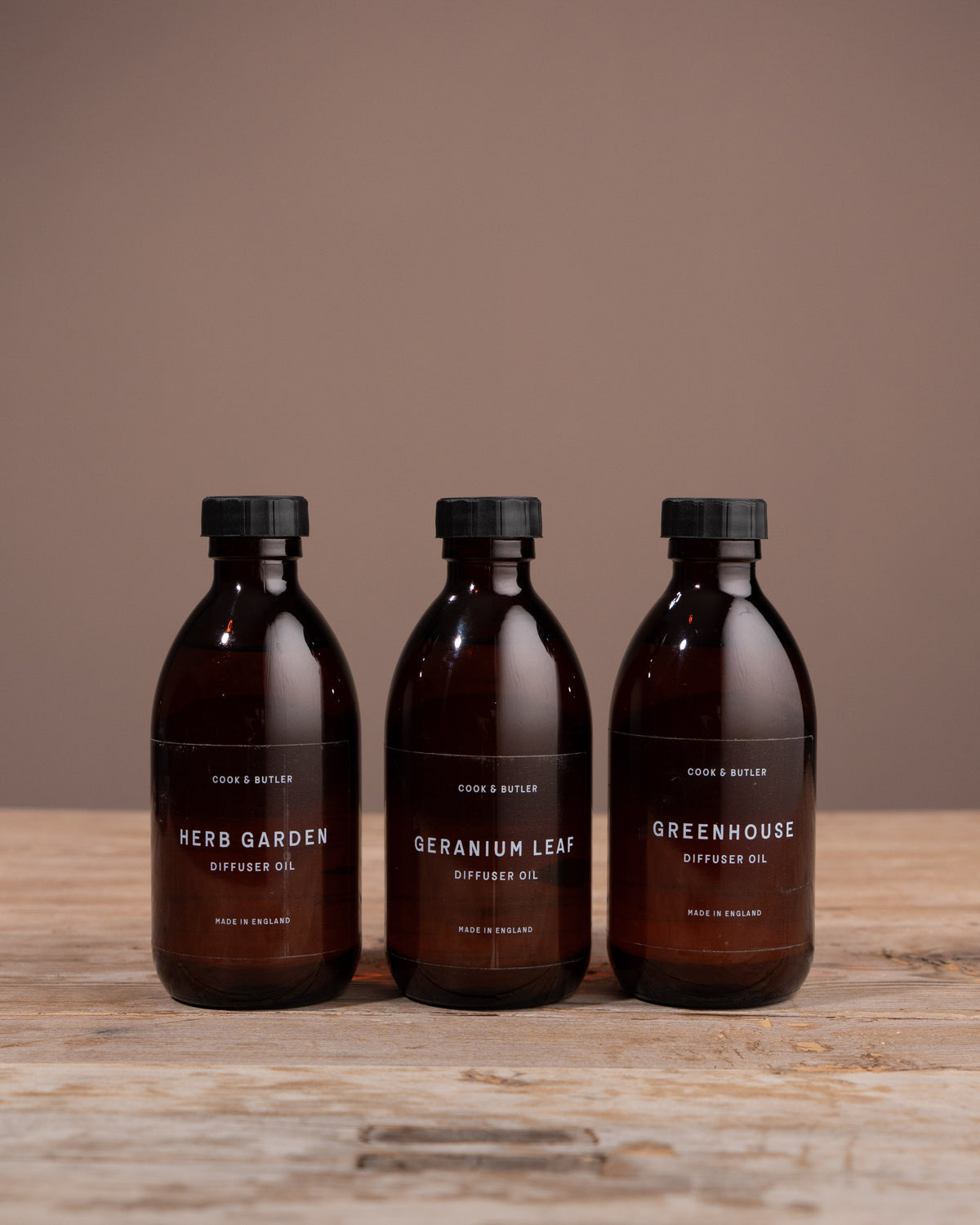 Three diffuser oil bottles from Caudle & Co. on a wooden surface with a brown background