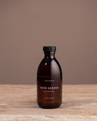 Bottle of Cook & Butler Herb Garden diffuser oil on a wooden surface with a brown background