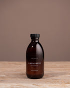 Bottle of Linen Press diffuser oil on a wooden surface with a brown background
