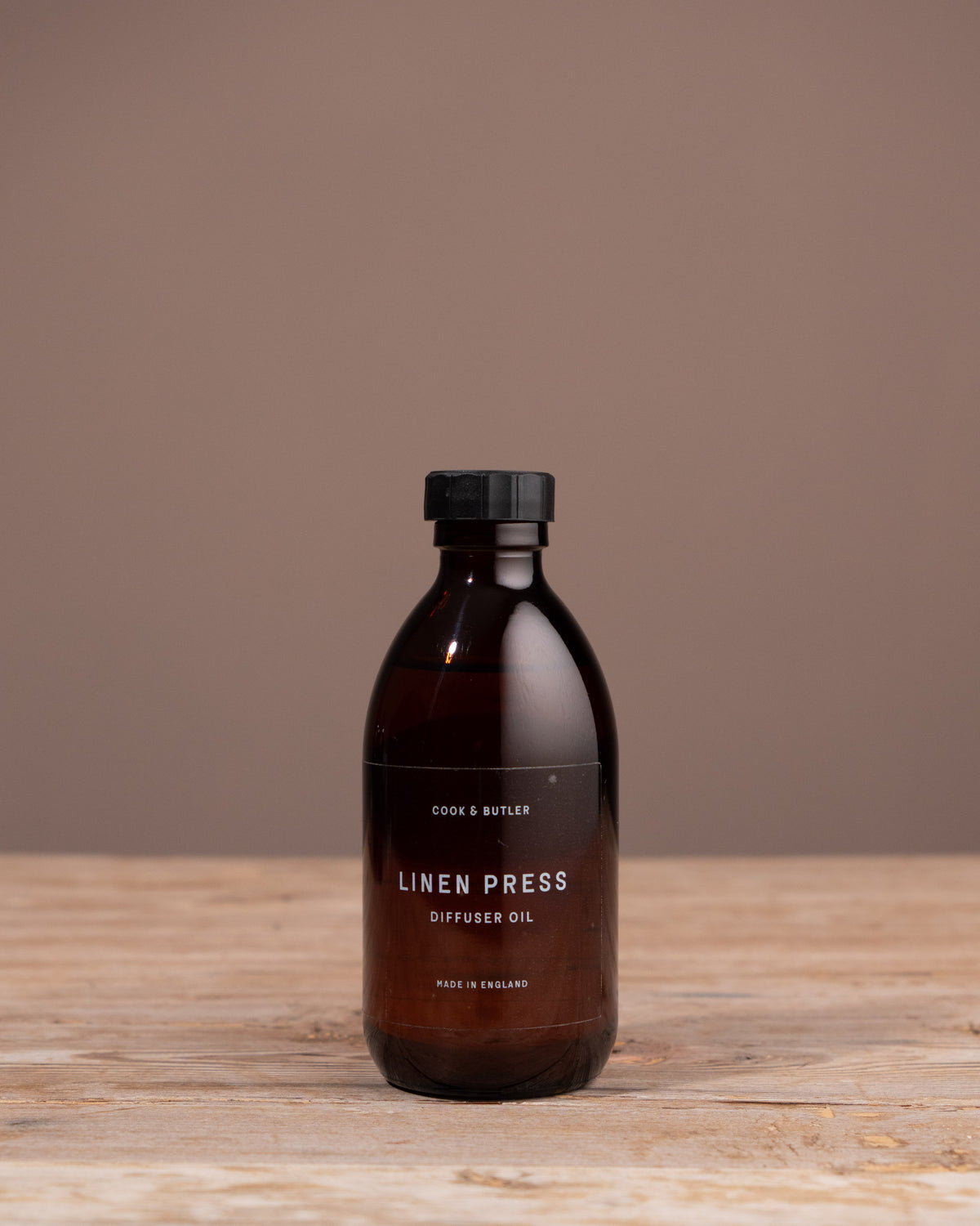 Bottle of Linen Press diffuser oil on a wooden surface with a brown background