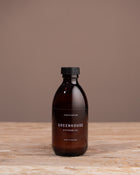 Bottle of 'Greenhouse' diffuser oil on a wooden surface with a brown background