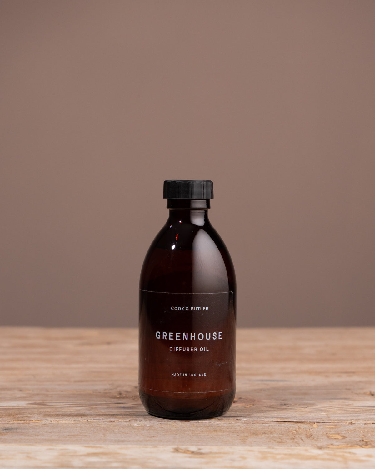 Bottle of 'Greenhouse' diffuser oil on a wooden surface with a brown background