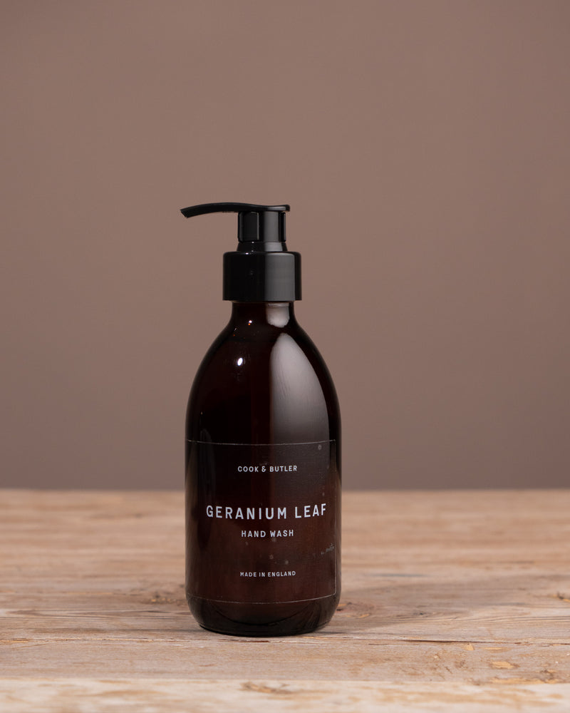 Brown hand wash bottle labeled 'Geranium Leaf' on a wooden surface with a brown background