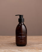 Brown bottle of 'Linen Press' hand wash on a wooden surface with a brown background