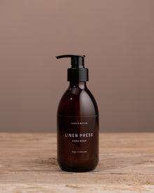 Brown bottle of 'Linen Press' hand wash on a wooden surface with a brown background