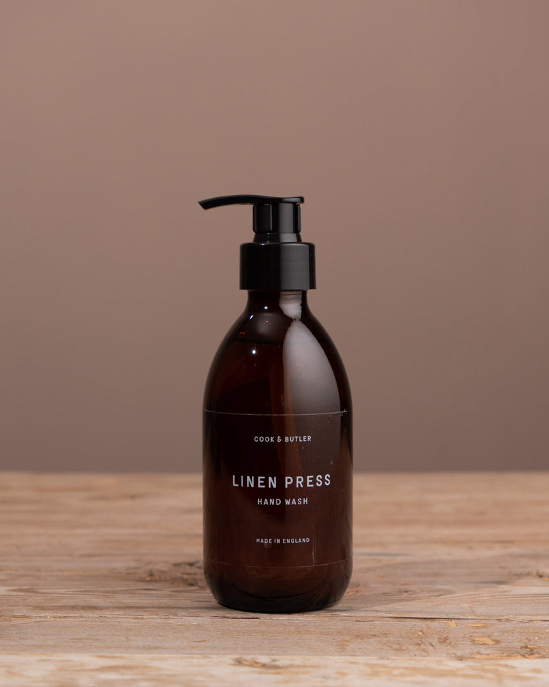 Brown bottle of 'Linen Press' hand wash on a wooden surface with a brown background
