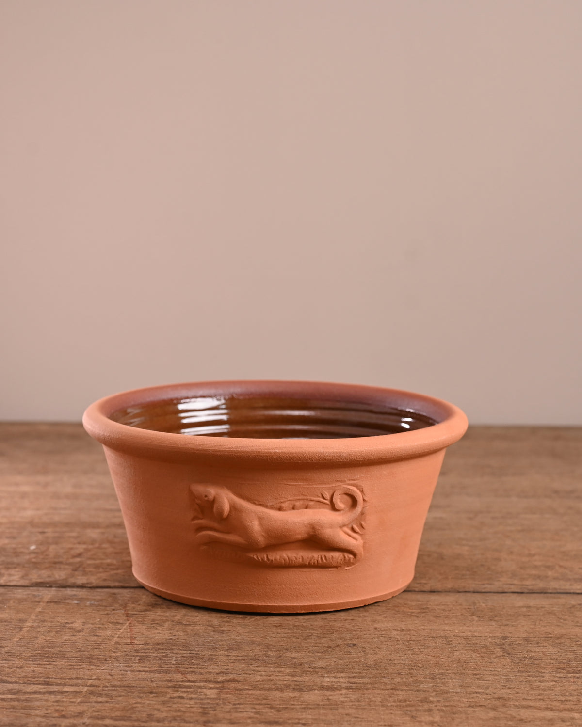 Terracotta pet bowl with dog design on a wooden surface