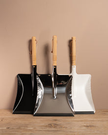 Set of three dustpans with wooden handles on a wooden surface against a beige wall.