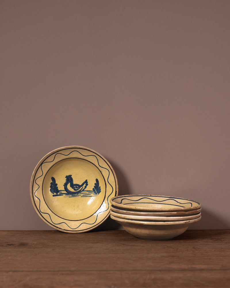 Set of ceramic plates with a cockerel design on a wooden surface against a brown background