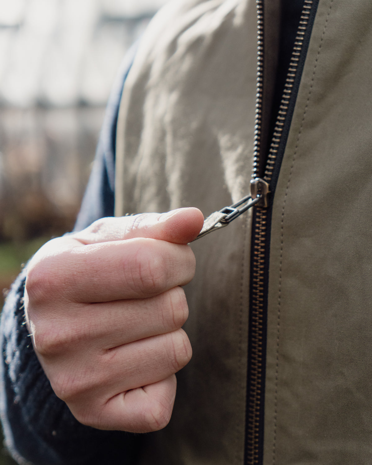 Hand zipping a beige jacket with a blurred background