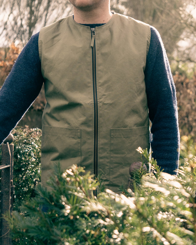 Person wearing a green vest over a dark long-sleeve shirt in an outdoor setting.