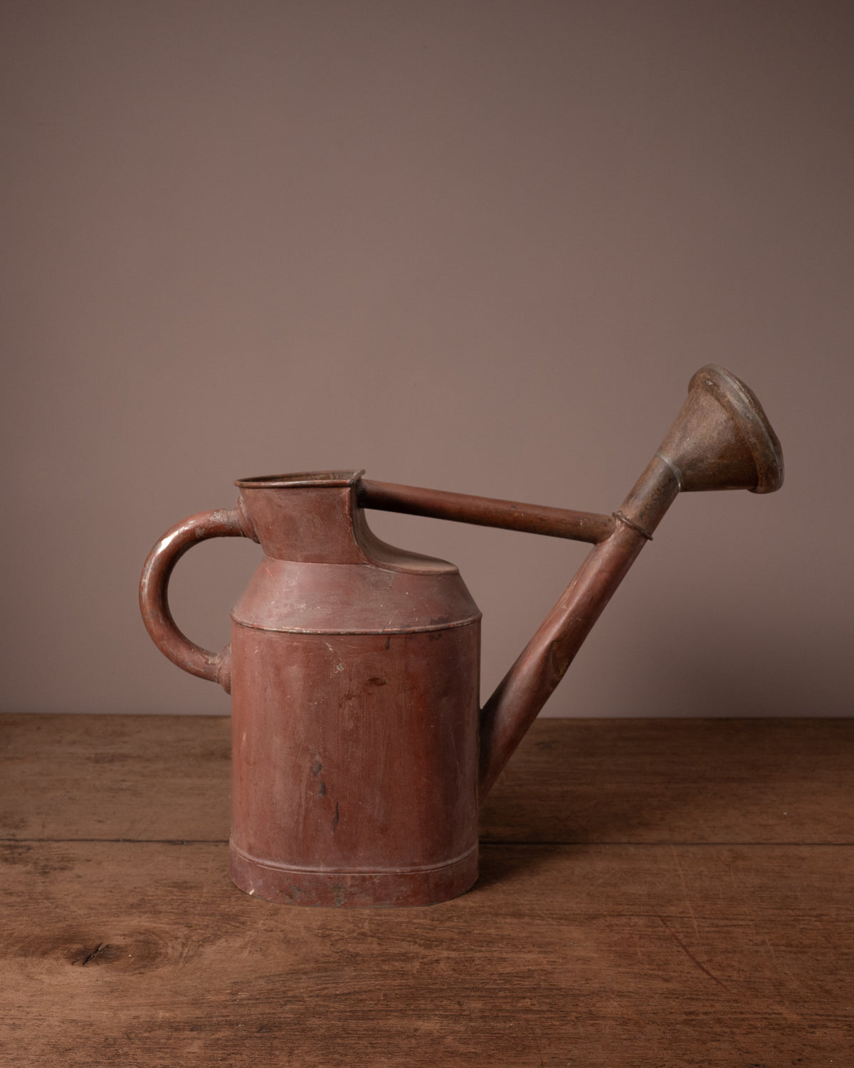 Vintage-style red watering can on a wooden surface with a brown background