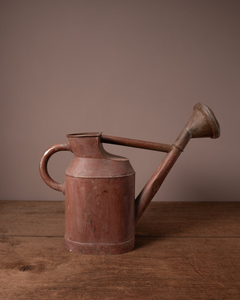 Vintage-style red watering can on a wooden surface with a brown background
