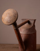 Vintage brown watering can with a textured handle on a wooden surface.