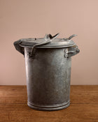 Vintage-style metal ash can on a wooden surface with a beige background