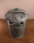 Vintage-style metal ash can on a wooden surface with a beige background