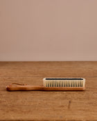 Handheld brush with wooden handle and bristle head on a wooden surface