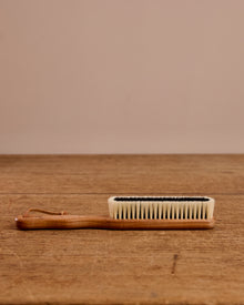 Handheld brush with wooden handle and bristle head on a wooden surface