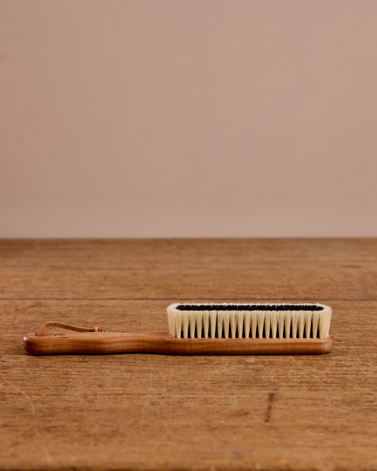 Handheld brush with wooden handle and bristle head on a wooden surface