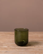 Green glass tumbler on a wooden surface with a brown background